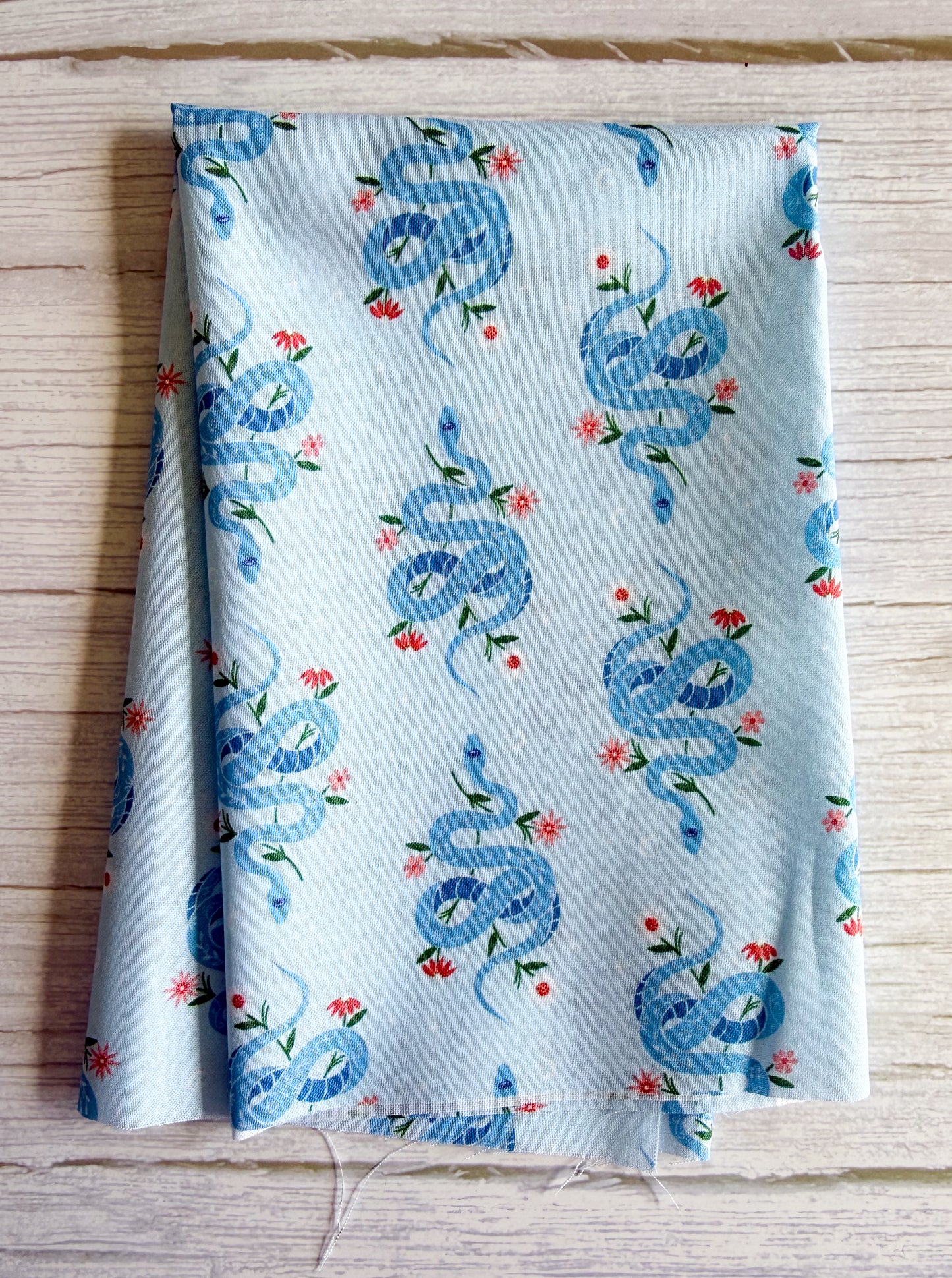 Fabric with blue snake pattern on a light blue background, folded on a wooden surface.