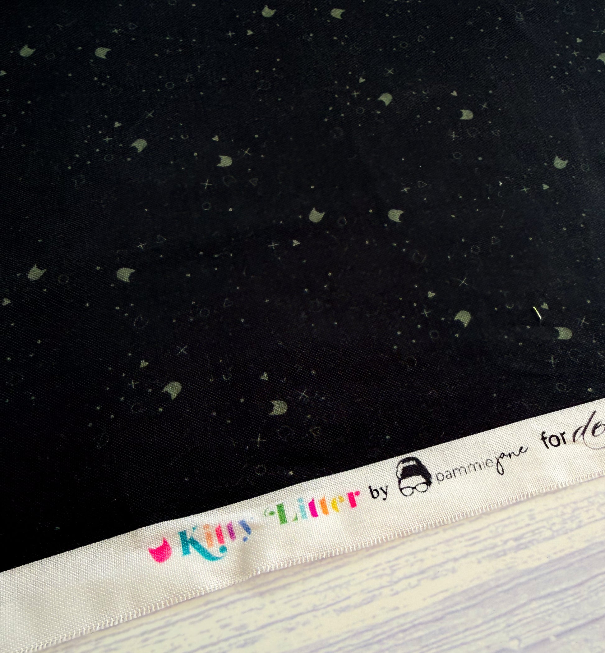 Black fabric with small gray shapes and a white label with colorful text.
