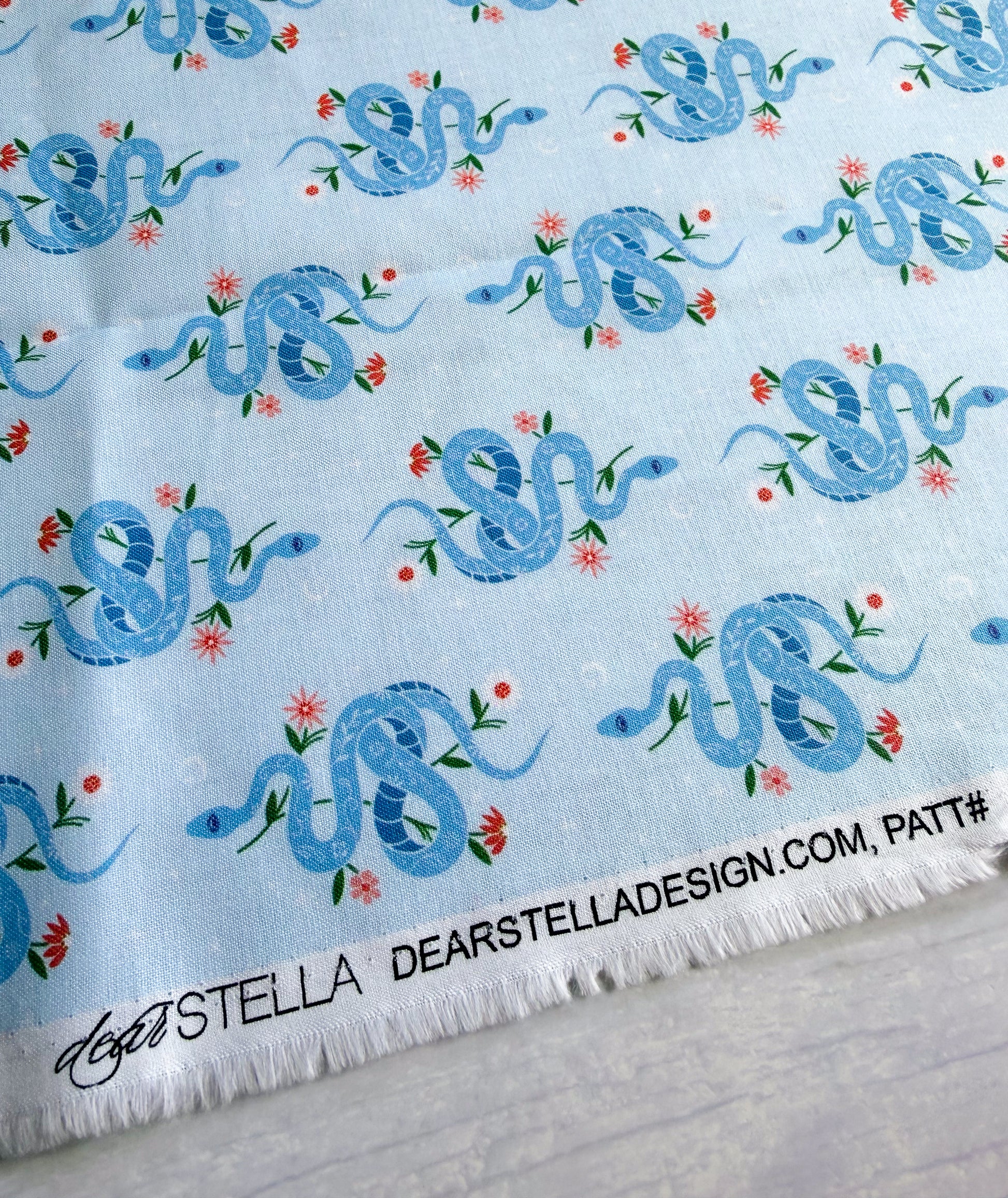 fabric with blue snake pattern on a light blue background, featuring the brand 'Dear Stella'.